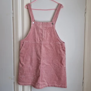 Rosa manchesterklänning Monki - Tjusig manchesterklänning i gammelrosa/puderrosa kulör. Bred manchester. Reglerbara hängslen i 2 olika lägen. Fickor. Når ungeför ner till mitten på låret. Nyskick! Anvönd en enda gång.  Passar M/40/42