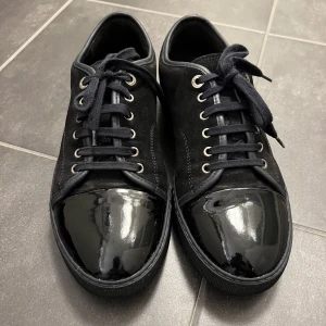 Lanvin skor - Lanvin dbb1 i svart mocka, glansig cap toe samt mörkblå/svart sula. Skorna är i använt skick och det medföljer inget annat än skor. Skicket är enligt mig 7/10, använda men en hel del liv kvar. Skorna är i storlek 7 vilket motsvarar 42 och mindre 43. 