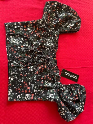 Oanvänd blommig offshoulder blus - Oanvänd top, offshoulder Kort  Blommig med svart grundfärg Volang i ringning, dragkedja 23 cm , bak  Resår upptill/nertill på ärmarna På etiketten står det EU FR 36 oEU DE 34 som storlek  100%polyester 