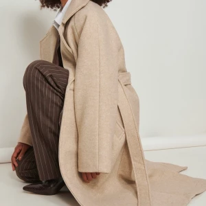 Lång beige kappa - Säljer denna otroligt fina kappa från nakd. Tjockt tyg och dubbelt så är som en vinterjacka. Oversized så passar storlek 34-40 beroende på hur man vill att den ska sitta. Köpt för 1200! 