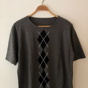 Argyle mönstrad topp/tröja - Grå t-shirt i "stickat" material med svart och vitt argyle mönster på mitten. Uppskattad storlek: L. Tveka inte att skicka privat vid någon fundering eller om du vill ha någon mer bild på plagget!!🤍