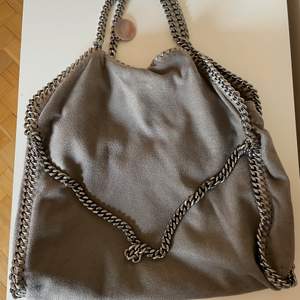 Snygg grå Stella McCartney väska i Falabella modellen. Det är medium storleken som är en najs vardagsväska. Jag har använt den en del därav det billiga priset. Lite slitningar här o där men inget större.