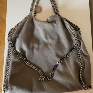 STELLA MCCARTNEY VÄSKA - Snygg grå Stella McCartney väska i Falabella modellen. Det är medium storleken som är en najs vardagsväska. Jag har använt den en del därav det billiga priset. Lite slitningar här o där men inget större.