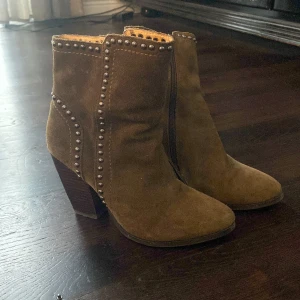 Högklackade boots med nitar - Högklackade boots med nitdetaljer från Buffalo London. Inköpta på Sellpy. Helt oanvända, prislapp sitter kvar. Grön/brun mocka. Klackhöjd ca 8-9 cm. Äkta mocka.