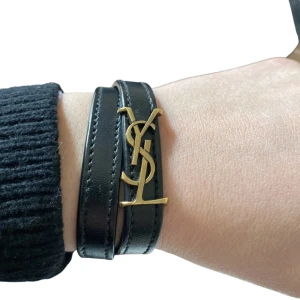 Ysl armband  - Säljer mitt så fina svarta Yves saint Laurent armband med guld detaljer. Armbandet är i storlek M. Armbandet är i fint skick. Köptes på ysl hemsidan, kvitto skickas digitalt vid köp. Alla tillbehören medföljer. 💗