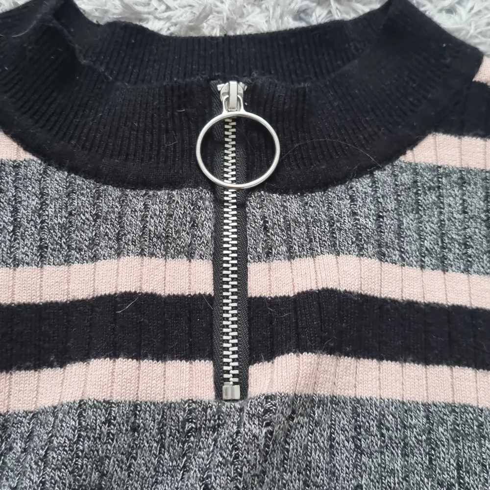 En randig tröja, med färgerna rosa, grå och svart. Den har en dragkedja vid halsen som funkar precis som den ska. Tröjan är från H&M och är helt i nyskick.. Stickat.