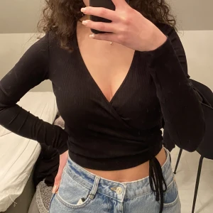 Tröja från Chiquelle  - Svart långärmad tröja från Chiquelle i storlek S. Materialet är ribbat och har omlott modell med en slags snörning. Knappt använd är i bra skick. 