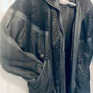 Vintage skinnjacka med snygga detaljer  - Svart skinnjacka från Otello Pelle storlek M, lite oversize. Inköpt i London.   Snygga detaljer med mönstring fram och bak, dragsko nertill, 2 fickor fram, kort krage.   Litet hål i ena fickan som enkelt kan sys igen, annars välbevarad. 