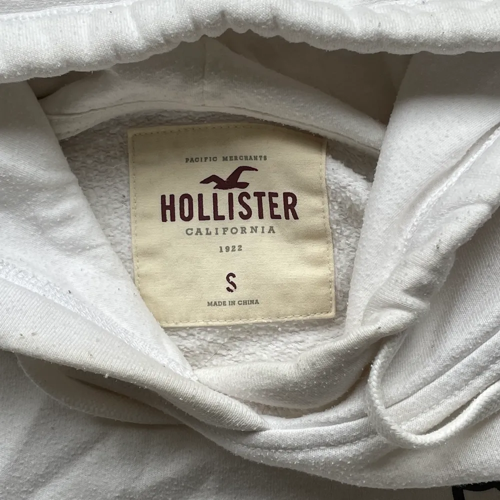 En vit hoodie med detaljer på i stolek S ifrån hollister. Är en magtröja och därav lite kortare. Längd: 40 cm. Fler bilder kan fås och kan skicka den!. Hoodies.