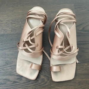 Beiga/puderfärgade klackar skor H&M 37 snörning - Beiga/puderfärgade högklackade sandaletter med grov klack och öppen tå, från H&M. Storlek 37. Använt men ok skick. Siden-imitations-material. Snörning runt ankeln.