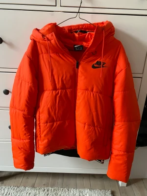 Orange Nike dunjacka - Orange dunjacka från Nike i storlek M. I bra skick. Med luva och dragkedjor vid fickor. 