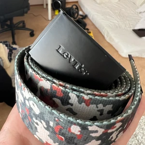 Levi’s Camo Belt - Ett skärp i polyester med ena sidan camo den andra mörkgrön. Bältet låses med klammermekanism. 
