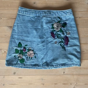 Jeanskjol - Jeanskjol med broderade blommor och dragkedja där bak. Använd 1 gång. 