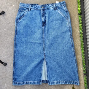 Lång jeanskjol - Jätte fin jeanskjol jag köpte för ett tag sedan som aldrig kom till användning. Kjolen är i nyskick och är använd endast 1 gång. Kjolen har en slit framtill och har en workwear/cargo stil. Den är i storlek L men är lite mindre i storlek.