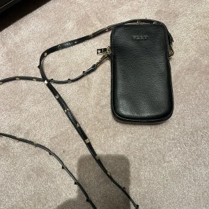 DKNY väska - Väska från DKNY. Svart med guldig text, nitar på bandet, ficka på baksidan och även flera små fack inuti! Köpt i USA o endast använd en gång.
