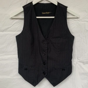 Kostymväst pinstripe - Svart figursydd kostymväst med vita ränder. Västen är inte stretchig, men den går att justera på ryggen. De tre fickorna är endast dekoration. Mycket bra skick. Om du har frågor eller vill se mer bilder är det bara att fråga!