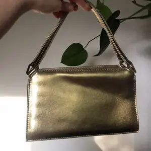Liten handväska från Jane Shilton / Clubhouse i guld. Osäker om det är äkta läder eller ej men den känslan iaf. Dragkedja, litet fack inuti och ett på baksidan. I fint skick. 