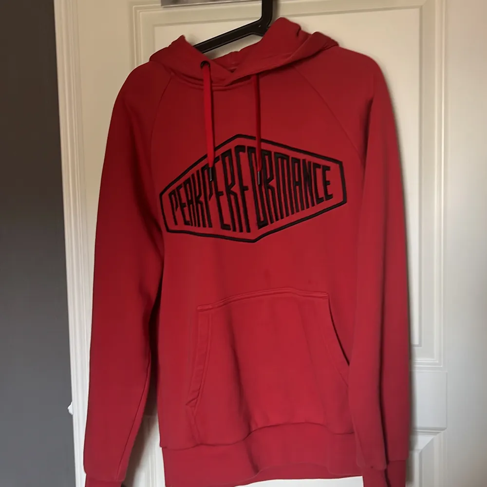 Röd peak performance tröja med svart text över bröstet. I storlek L, anser den vara liten i storleken så skulle sitta perfekt på en storlek M. Köpt för 3 år sedan men knappt använd.. Hoodies.