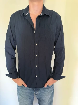 Mörkblå skjorta från Jack & Jones - Säljer en stilren mörkblå skjorta från Jack & Jones med klassisk krage, bröstficka och vita knappar. Fint skick. Hör av dig om du har några frågor eller vill ha fler bilder. Pris kan diskuteras! 