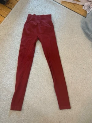 Vinröda höga leggings - Säljer ett par vinröda leggings med hög midja och smal passform. De är stretchiga och mjuka, perfekta för en avslappnad look. Materialet ser ut att vara bomull eller en bomullsblandning. Passar dig som gillar bekväma och stilrena plagg.