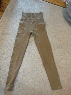 Beige ribbade leggings med hög midja - Säljer ett par beige leggings med ribbad struktur och hög midja. De har en tight passform och långa ben, perfekta för en chill och trendig look. Materialet känns mjukt och stretchigt, vilket gör dem riktigt bekväma att bära.