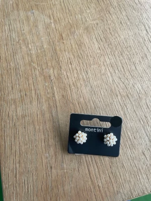 Pärlörhängen från Montini - Söta örhängen från Montini med små vita pärlor formade som blommor. Perfekt accessoar för att ge en söt och klassisk touch till din stil. Fästs med stift och har en elegant design som passar till många olika looks.