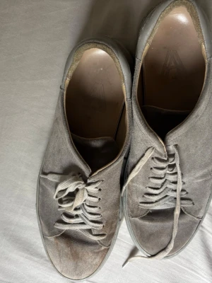 Grå mockasneakers med snörning - Snygga sneakers i grå mocka med klassisk låg profil och matchande grå snören. Yttersulan är i gummi och har ett diskret randigt mönster undertill. Perfekta för en clean och stilren look till vardagsoutfiten.
