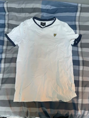 Jack and Jones t-shirt - Vit t-shirt med mörkblå kant vid hals och ärmslut samt en liten gul broderad logga på bröstet. Klassisk passform och korta ärmar, perfekt till vardagslooken. Tillverkad i mjuk bomull för skön känsla.