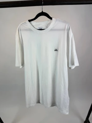 Vit t-shirt från C.P. Company - Säljer en stilren vit t-shirt från C.P. Company med liten logotyp på bröstet. T-shirten har klassisk passform, rund hals och korta ärmar. Perfekt basplagg i mjuk bomull som funkar till allt.