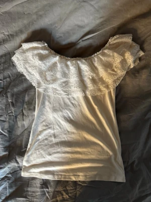 Vit offshoulder topp med spets - Supersöt vit offshoulder topp från May by Shining Star. Toppen har bred volang med spetsdetaljer runt axlarna och är tillverkad i mjukt bomullsmaterial. .