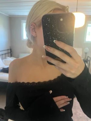 Svart offshoulder topp med spetskant - Säljer en svart offshoulder topp med lång ärm och fin spetskant längs urringningen. Toppen har en slim passform och är perfekt för dig som vill ha en enkel men snygg look. Materialet känns mjukt och stretchigt.