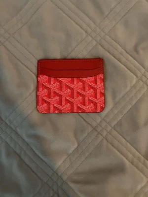 Röd kortfodral med grafiskt mönster - Snyggt rött kortfodral med ett grafiskt mönster i vitt och rosa. Fodralet har flera kortfack och är tillverkat i ett tåligt material som ser ut som canvas med detaljer i läder. Perfekt för dig som vill ha ett stilrent och trendigt accessoar.