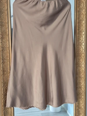 Beige kjol i satin - Snygg beige midikjol i satin med lätt glansig finish och enkel, stilren design. Kjolen har en mjuk och följsam passform. Använd fåtal gånge
