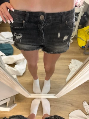 Svarta slitna jeansshorts - Xxs-xs, kanske passar S. Säljer ett par svarta jeansshorts med slitningar och rå kant nertill. Shortsen har fem fickor, knappgylf och en cool, tvättad look. Perfekta för dig som gillar en avslappnad och trendig stil.