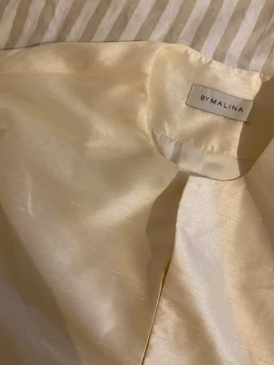 Krämvit glansig kofta från By Malina - By Malina blus, sparsamt använd i storlek xs den är krämvit men skulle säga att den drar lite åt det ljusgula hållet. 