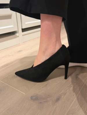 Svarta pumps från NLY Shoes - Stilrena svarta pumps från NLY Shoes med spetsig tå och hög smal klack. Skorna är i mockaimitation och har en klassisk siluett som passar till många olika outfits. Storlek 35, aldrig använda endast testade inomhus. 