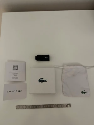 Lacoste klockarmband i silver - Säljer ett stilrent klockarmband från Lacoste i silverfärgad metall. Medföljer originalförpackning, tygpåse och extra länkar. Perfekt för dig som vill byta ut eller förlänga ditt armband på din Lacoste-klocka.