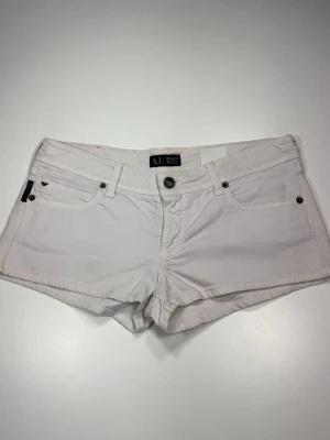 Vita shorts från Armani Jeans - Säljer ett par vita shorts från Armani Jeans med klassisk femficksdesign och knappgylf. Shortsen har AJ-logga på bakfickan och patch bak i midjan. Perfekta för varma dagar och har en snygg, enkel look. 0039