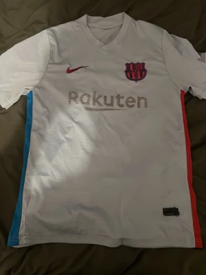 Ljus lila FC Barcelona matchtröja Nike - Säljer en ljus lila FC Barcelona matchtröja från Nike med klubbmärke och röd Nike-logga på bröstet. Tröjan har Rakuten-tryck fram och UNICEF-tryck bak samt blå och röda ränder längs sidorna. Perfekt för dig som älskar fotboll och Barca!
