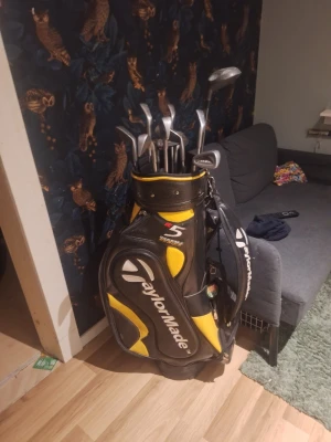 Måste hämtas på plats skriv dm vi intresse, TaylorMade golfset med bag - Säljer ett komplett golfset med flera järnklubbor som järn 2a till järn 9a även pitch o sand och en svart och gul TaylorMade golfbag man får även med bollar o peggar. Bagen har axelrem och flera fack för tillbehör. Perfekt för dig som vill börja spela golf eller behöver ett extra set.
