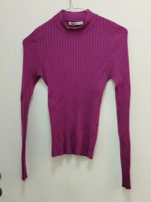 Ribbad lila polotröja - Säljer en ribbad lila polotröja med lång ärm och figurnära passform. Tröjan har en krage och är tillverkad i ett stretchigt material som sitter snyggt på kroppen. Perfekt för lager på lager och enkel att styla till olika outfits. Se mått på bilder och se gärna mina andra annonser <3