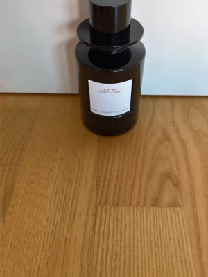 Parfait d'Orchidée  - En elegant parfymflaska från Zara med namnet Parfait d'Orchidée. Flaskan är mörkbrun och har en stilren, rund form med svart lock. Etiketten är vit med svart text. Perfekt för dig som gillar blommiga dofter.
