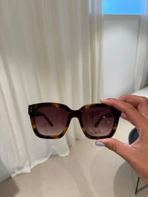 Solglasögon från Corlin - Snygga solglasögon i fyrkantig modell från Corlin i modellen MODENA med brunmelerad båge och tonade linser. Bågarna har en klassisk och trendig look!