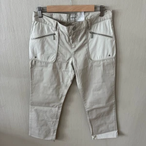 Calvin Klein Beige cargobyxor med dragkedjor - Snygga beige cargobyxor med raka ben och två stora fickor framtill med dragkedjor. Byxorna har även en bakficka och bälteshällor. Tillverkade i ett mjukt bomullsmaterial som ger en avslappnad look. 0383