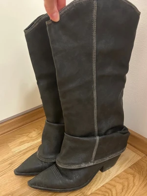 Cowboy Boots - A pair of black cowboy boots with pointed toes and a folded-over shaft. The boots have a classic western style with a mid-height heel and visible stitching. They are being held upright by a hand.
