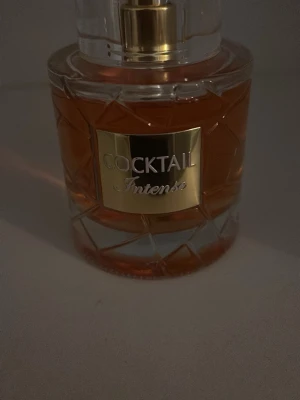 Cocktail Intense parfymflaska - Cocktail Intense parfym i en elegant, rund glasflaska med guldigt lock och detaljer. Vätskan är bärnstensfärgad och flaskan har ett mönstrat glas som ger en lyxig känsla. Perfekt för dig som gillar exklusiva dofter.
