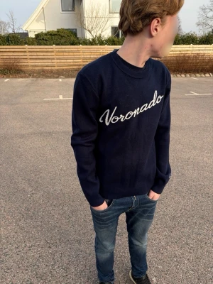 Mörkblå stickad tröja Voronado - Snygg mörkblå stickad tröja från Voronado med vit broderad logga över bröstet. Tröjan har rund halsringning och långa ärmar. Perfekt till jeans för en avslappnad men stilren look.