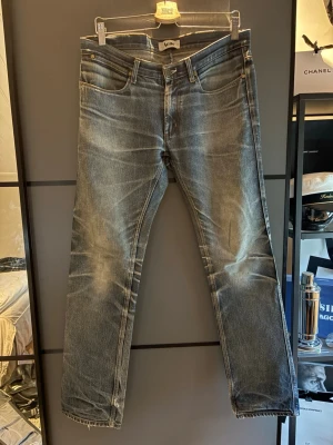 Blå raka jeans från Acne Studios - Säljer ett par blå raka jeans från Acne Studios med slitna detaljer och ljusa tvättade partier. Jeansen har klassisk femficksmodell, normal midja och råa kanter vid bensluten. Perfekta för en avslappnad och trendig look.