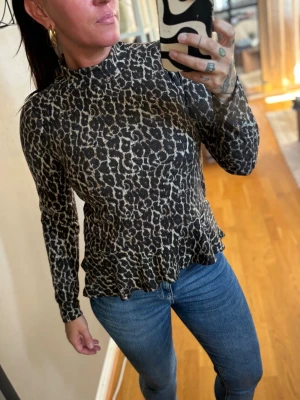 Leopardmönstrad långärmad topp - Snygg långärmad topp med leopardmönster och hög hals. Toppen har en lätt figurnära passform och volangkant nedtill. Perfekt för dig som vill sticka ut lite extra med ett djurmönster. St 34 men jag har S och passar