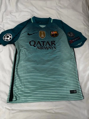 Barcelona Neymar Jr matchtröja - Snygg Barcelona matchtröja i turkos och svart med Neymar Jr och nummer 11 på ryggen. Tröjan har klubbmärke, Qatar Airways-tryck, Champions League och FIFA-märken samt Unicef-logga. Tillverkad i lätt och ventilerande material, perfekt för fotboll eller träning.